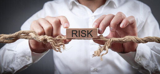 Man with a frayed rope showing Risk word on wooden block. Risk - obrazy, fototapety, plakaty