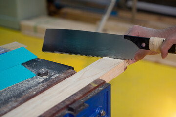 Professional carpenter man is sawing a wooden beam in woodwork industry. The worker makes a cut on a  saw.
