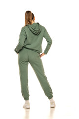 Rear view of a young woman in a green tracksuit posing to a white background in the studio.