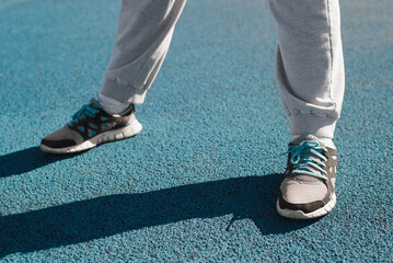 Close-up of woman's legs in sneakers standing on rubber surface of an outdoor sports field on sunny day