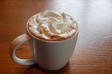 Closeup hot mocha fresh coffee in a white cup with whipping cream on wooden table background. Drink...