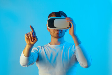 Modern young man experiencing virtual reality glasses in futuristic neon illuminated studio
