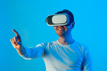 Modern young man experiencing virtual reality glasses in futuristic neon illuminated studio
