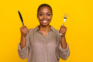 Photo of positive funny lady dressed checkered shirt holding silver fork knife isolated yellow color background