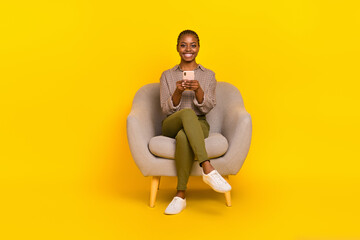 Photo of positive cute lady dressed checkered shirt sitting chair chatting modern gadget isolated yellow color background