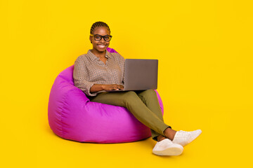 Photo of sweet pretty lady dressed checkered shirt sitting bean bag working modern gadget isolated yellow color background