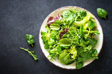 Green salad leaves in white plate on black background. Top view image.
