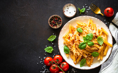 Pasta with tomato sauce, basil and parmesan on dark stone table. Penne pasta with tomato sauce alla arrabbiata. Top view.