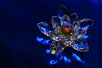 Crystal lotus on rich dark blue shiny table with light reflection.