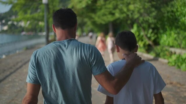 Father and son walking together at park dad with arm around kid bonding family time
