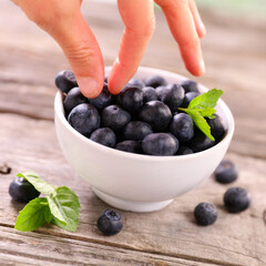 bowl of fresh blueberry fruit with hand holding a blueberry