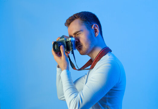 Contemporary young man posing in various poses in studio.Futuristic neon lighting.Taking pictures with analog camera