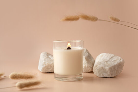 Vanilla burning candle on beige background. Warm aesthetic composition with stones and dry flowers. Home comfort, spa, relax and wellness concept. Interior decoration