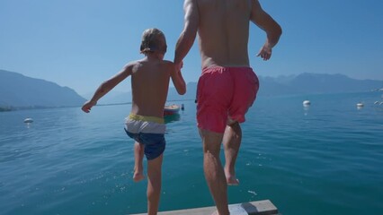 People diving into water in super slow motion father holding hands with son running together jumping into lake - Powered by Adobe
