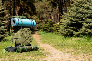Tourist backpack standing near the path leading to the forest. Concept: The beginning of the hike.
