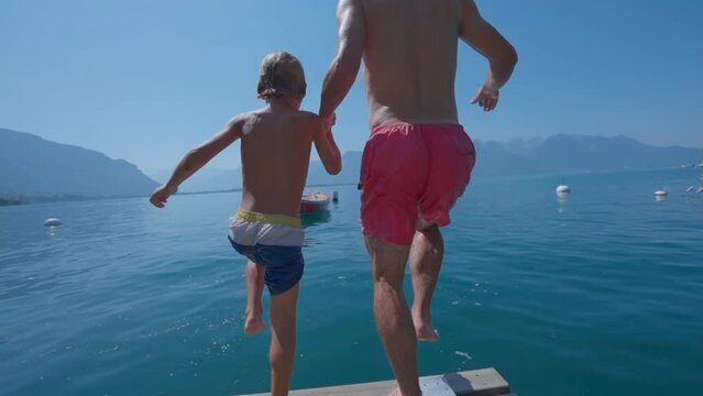 People diving into water in super slow motion father holding hands with son running together jumping into lake