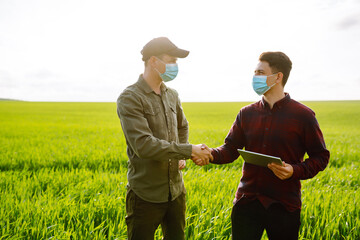 Farmers with tablet in the field. Farmers in sterile medical masks discuss agricultural issues on the field. Covid-19.