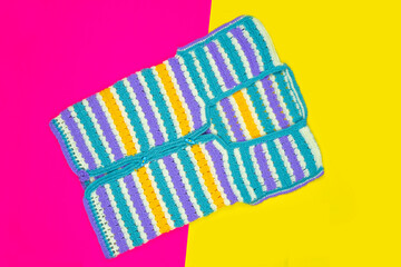 Colorful knitted sweater isolated on pink and yellow background, hand knitting cloth, top view of sleeveless jacket, yellow purple blue white sweater