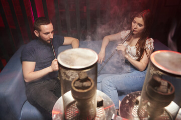 a young couple smokes a hookah in an atmospheric hookah lounge in a relaxed atmosphere, in front of a hookah with a protective screen on the coals