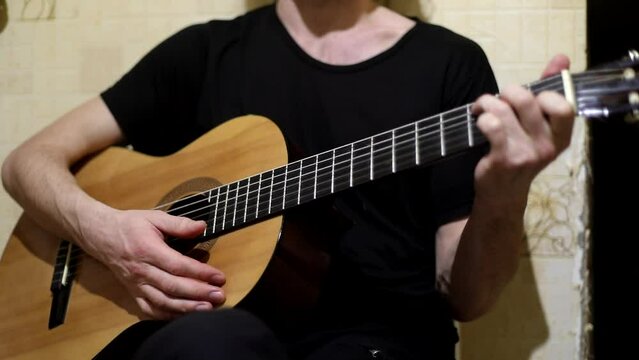 Guy plays guitar. Music lesson. Man in black T-shirt sorts through strings. Acoustic instrument.