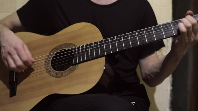 Guy plays guitar. Music lesson. Man in black T-shirt sorts through strings. Acoustic instrument.