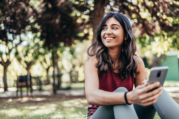 beautiful indian ethnicity young woman using mobile phone sitting in park