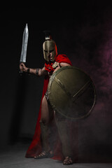 A young athletic man dressed as a Roman soldier in a red cloak and helmet stands full-length...