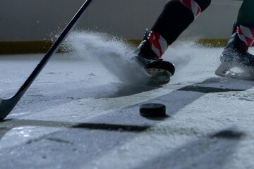 A hockey player slides across the arena and hits the puck with a hockey stick, cutting the ice into powder. Match on ice rink. Hockey training in a sports school, hitting the puck. Close up.