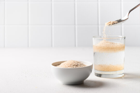 Woman adds psyllium fiber to glass of water on white background. Superfood for healthy intestines and gluten free diet, boosts weight loss.