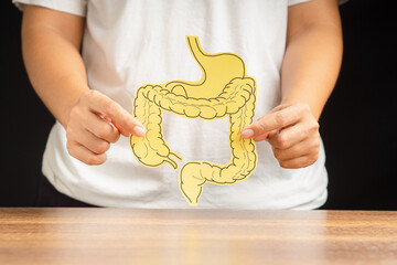 Hand holding a large intestine shape made from paper while standing over a black background