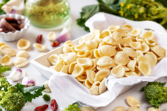 Orecchiette con cime di rapa ingredients typical of Apulia regional cuisine - homemade fresh pasta, turnip greens, chilli pepper, garlic and anchovy at the background