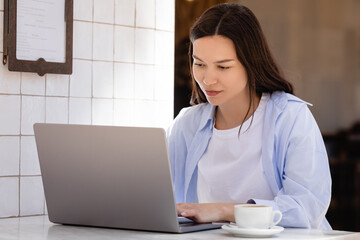 woman in blue shirt typing on laptop near coffee cup on cafe terrace.