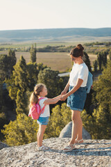 Fototapeta na wymiar Vertical portrait of happy mother and little daughter spend time together, hiking and enjoy the beautiful summer nature landscape