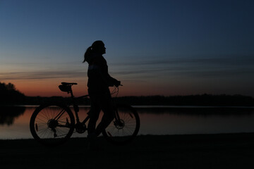 Fototapeta premium Silhouette of woman with mountain bike on colorful blue sky sunset background. Active outdoors lifestyle 