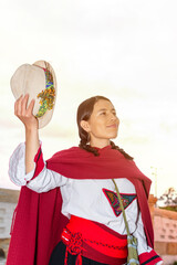 Naklejka premium Latin woman in peasant dress holding her hat with a colonial bridge in the background