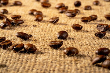 Fototapeta na wymiar Brown freshly roasted coffee beans on burlap cloth. Coffee seeds laid out on a textured fabric with interlaced fibers. Food and drink background. Aromatic beans of Robusta or Aribica. Close up.