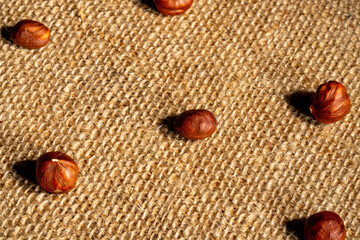 Brown peeled hazelnuts on a burlap cloth. Top view of round nuts close up. Hazel seed laid out in rows on a textured fabric with interlaced fibers. Dry hazel, healthy nuts, nutritious snack.
