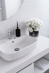 Fototapeta premium Electric toothbrush, flowers and white sink in bathroom