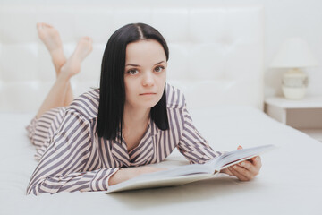 Obraz premium Barefoot young teenage girl looking at the camera lying on her bed reading a book
