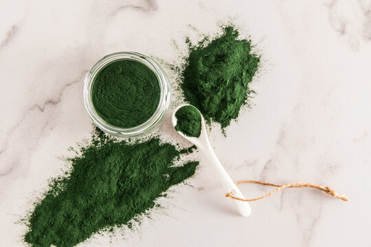 Organic green spirulina algae powder in a large glass jar on a marble table. top view. supplements to promote health.