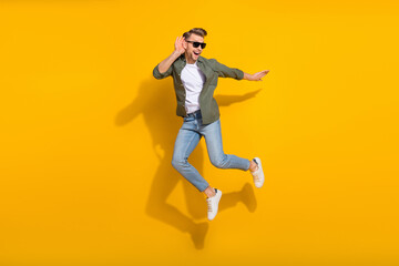 Naklejka na ściany i meble Full length body size view of attractive cheerful curious guy jumping listening isolated over bright yellow color background