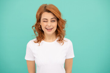 Obraz premium winking redhead woman with curly hair on blue background