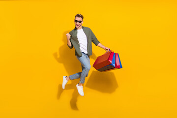 Fototapeta na wymiar Full length body size view of attractive cheerful guy jumping buying gifts things rejoicing isolated over bright yellow color background