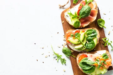 Foto op Canvas Open sandwichset met roomkaas, prosciutto, zalm, avocado en verse groenten. Bovenaanzicht aan witte tafel. Detailopname. © nadianb