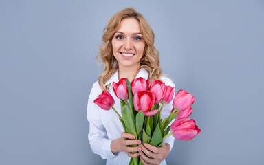 happy young woman holding spring tulip flowers on grey background