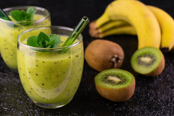 Two glasses with kiwi smoothie and banana on a black background.Close-up.
