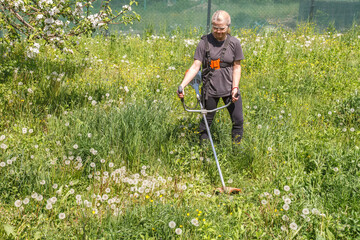 A woman mows grass on his property with a gasoline trimmer