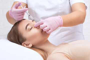 The doctor does injections to correct the hump on the nose. The beautician doeses injections against wrinkles on the face. Women's cosmetology in a beauty salon.
