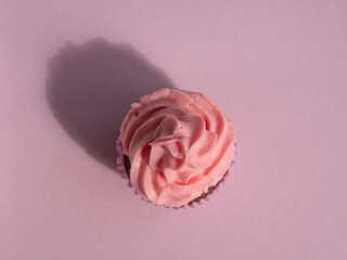 Cupcake on a pink background with a cap of cream, hard shadow, top view