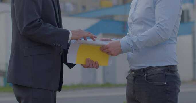 Two unrecognizable men met to pass on information security. Sale of classified data. Documents and files, its level of sensitivity. Hand gesture denoting money.